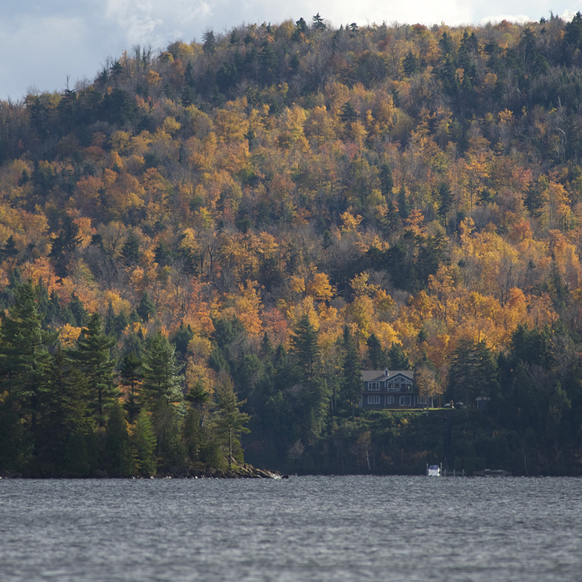 Maison isolée entourée de forêt aux couleurs de l'automne et d'un lac
